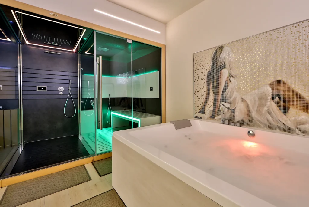 Nell'immagine il centro benessere dell'hotel. Al centro c'è una vasca idromassaggio con un mosaico sulla parete dietro. A sinistra si vede il bagno turco e le docce emozionali .